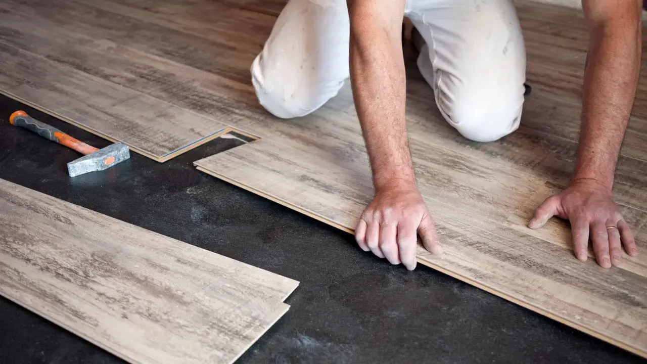 Pose de parquet flottant : un artisan installe des lames de bois sur un sol noir. Le prix de pose est une préoccupation pour ce type de revêtement.