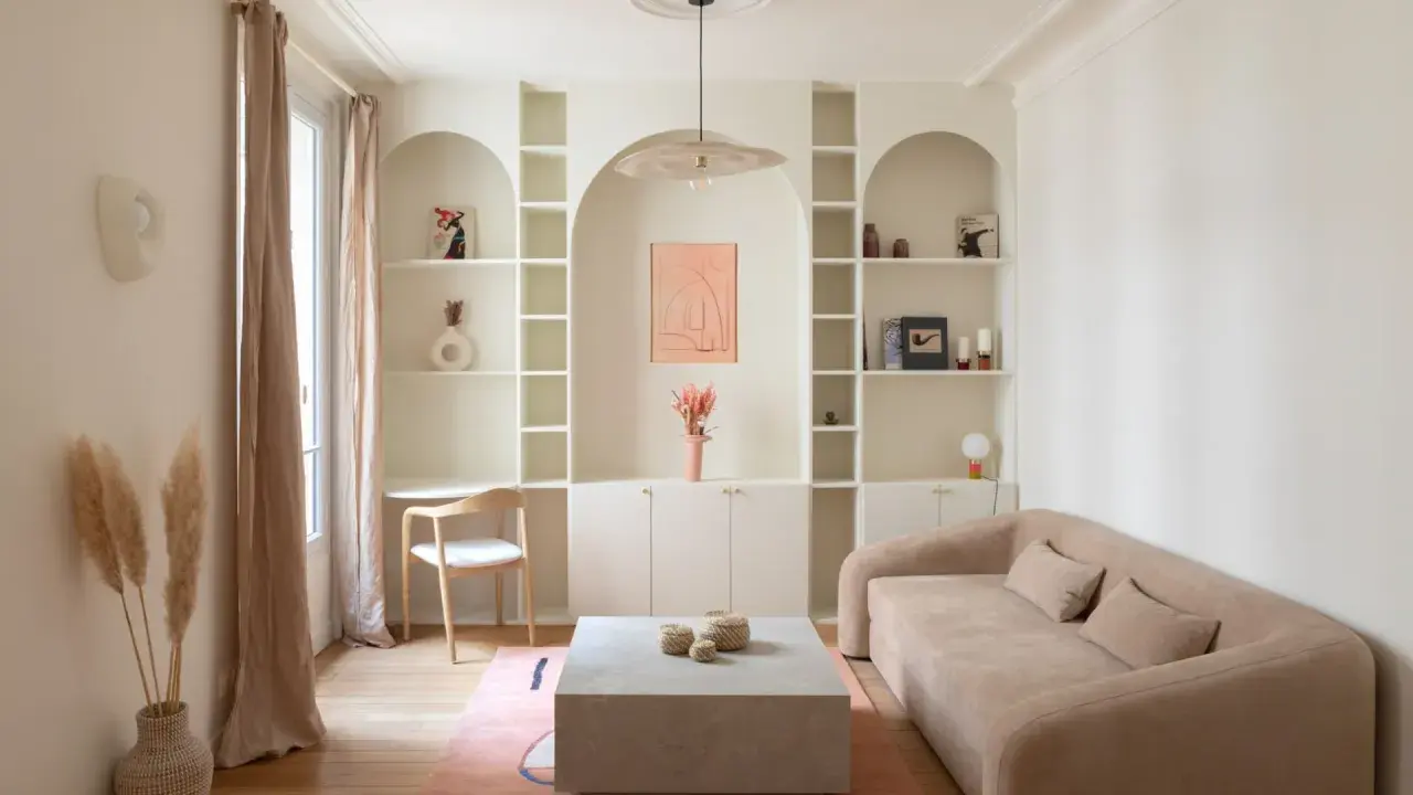 Un coin bureau discret dans un salon cosy, avec une étagère murale arche, un canapé beige et un tapis rose.