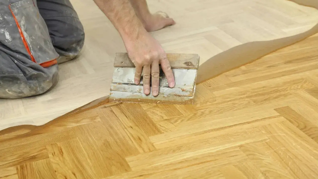 Un artisan applique un produit sur un parquet en chevrons. Une étape essentielle pour la réparation parquet.