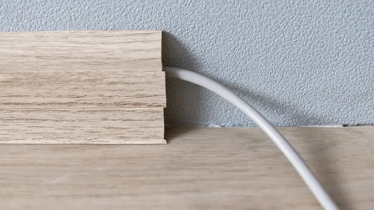 Une plinthe en bois imite le bois et cache un fil électrique. Astuce pour comment cacher des fils électriques.