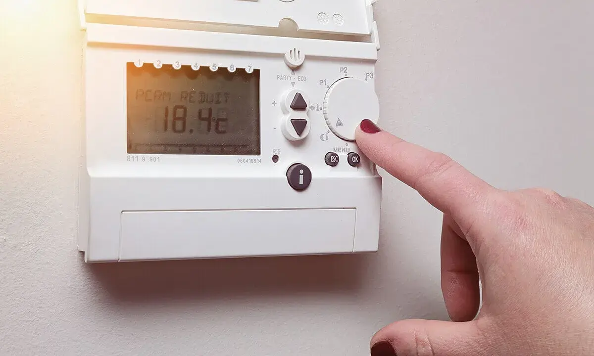 Main d'une femme ajustant un cee thermostat connecté affichant 18.4°C.