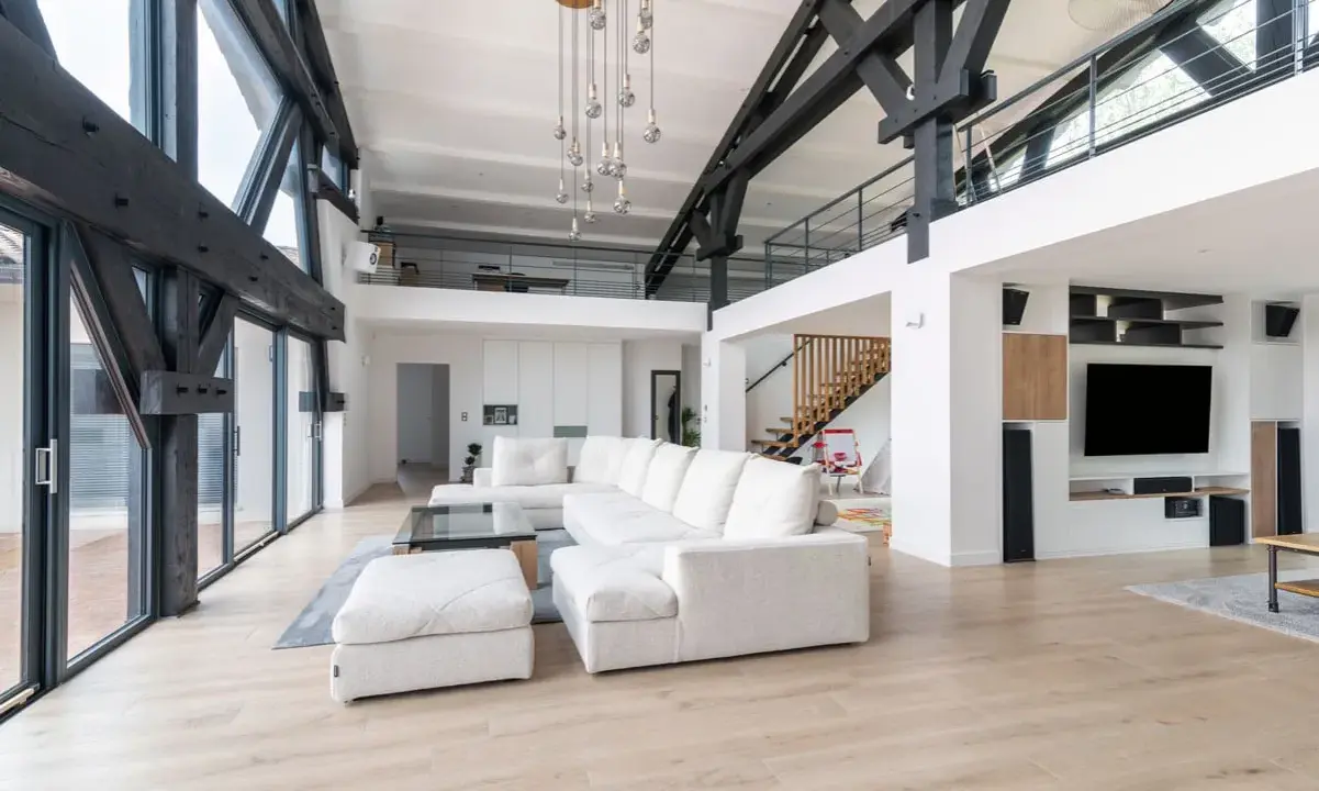 Salon moderne avec poutres apparentes, canapé blanc, escalier en bois. Ce style peut influencer le prix renovation appartement.