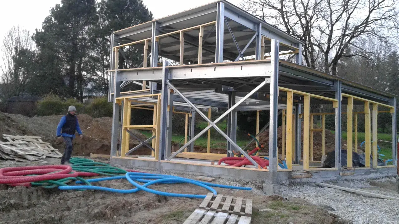 Chantier d'une maison ossature métallique. Le prix est un facteur clé pour ce type de construction moderne. Des tuyaux colorés sont visibles au sol.
