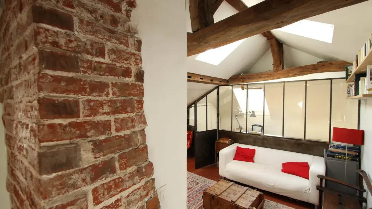 Aménagement combles idées : un salon cosy sous les toits avec murs en briques apparentes, poutres en bois et canapé blanc.
