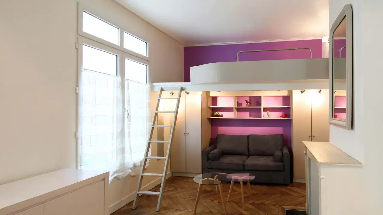 Un studio optimisé de plan 20m2 avec lit mezzanine, canapé, étagères violettes et échelle.