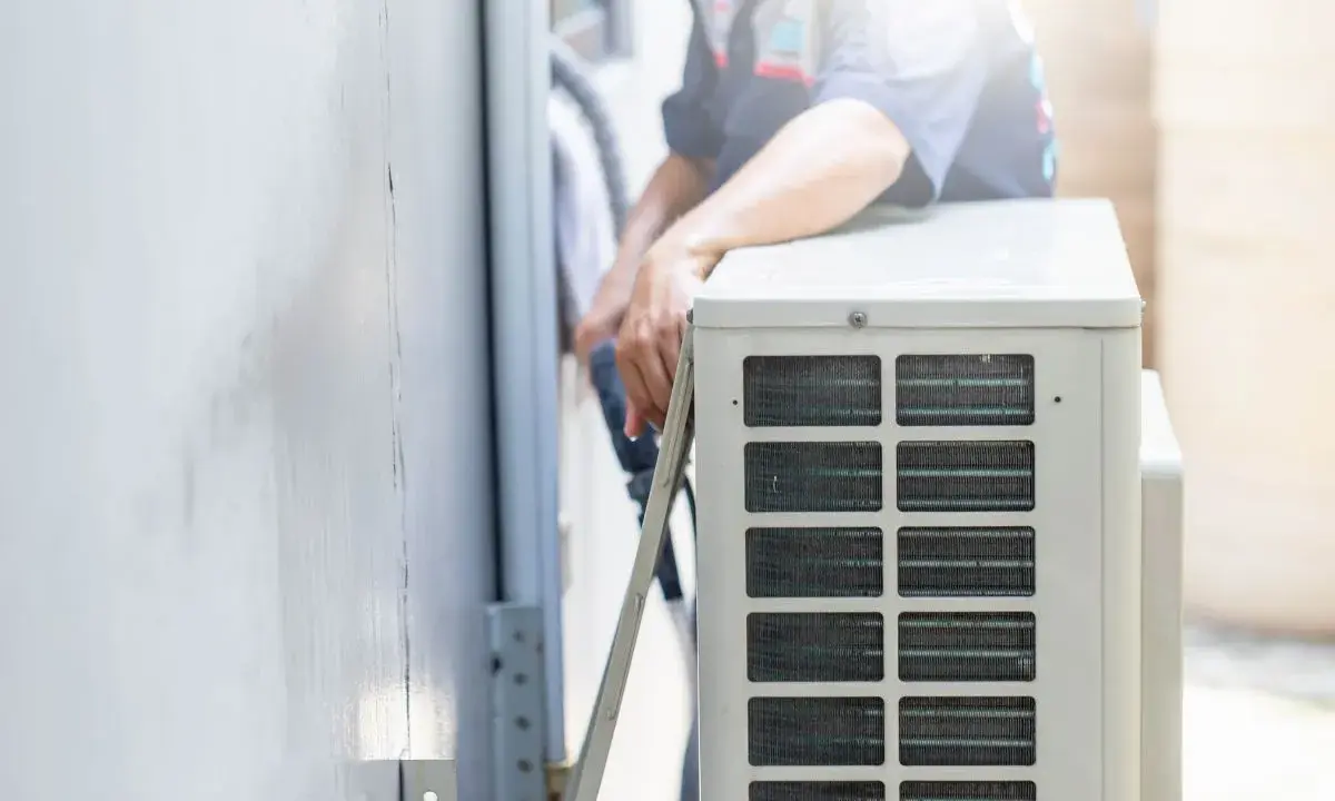 Un technicien s'occupe de recharger la clim de la maison. Il manipule des tuyaux près de l'unité extérieure.