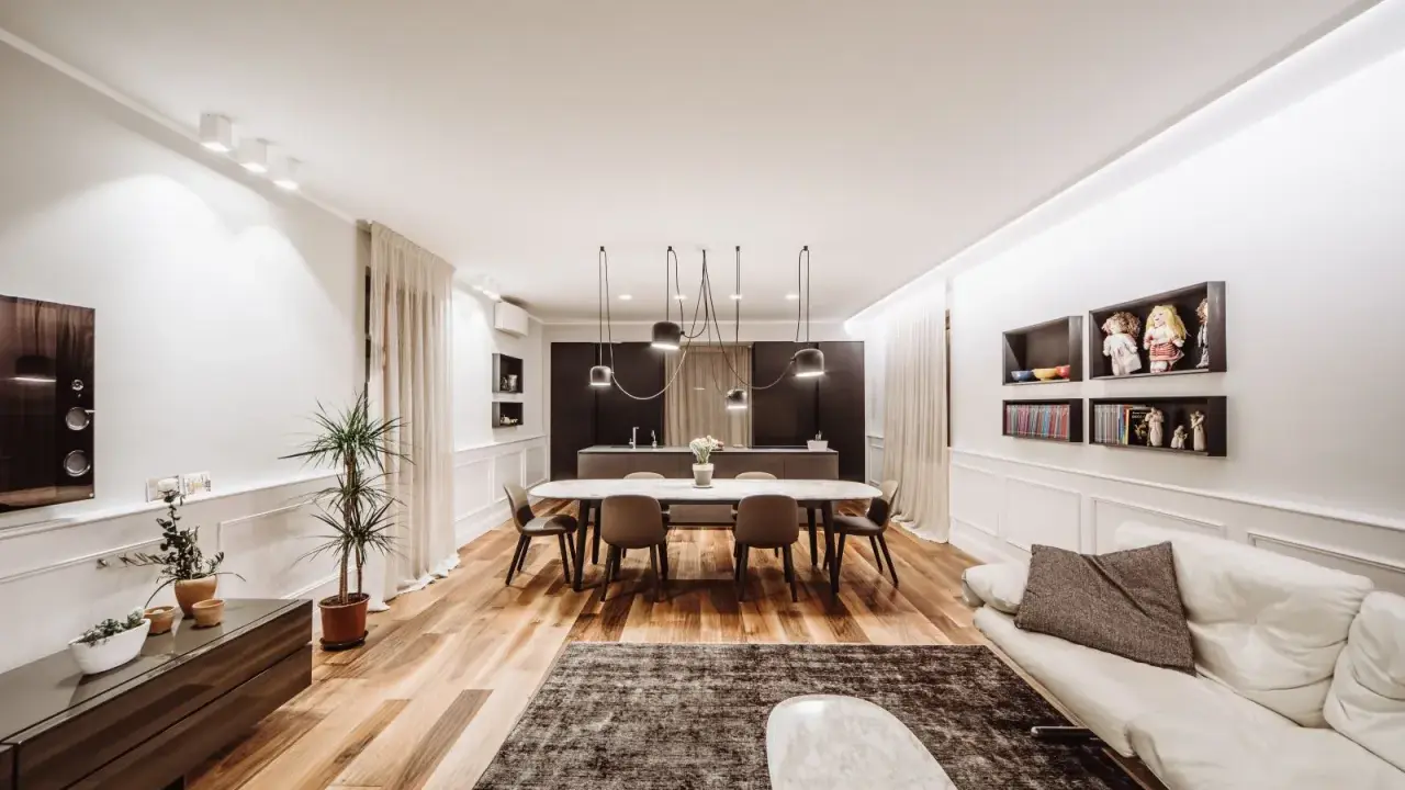 Un grand salon moderne avec un canapé blanc, une table à manger ovale et une cuisine intégrée. La taille du salon est optimisée pour le confort.