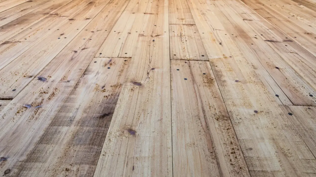 Planches de bois clair, usées et clouées, avec un parquet qui craque sous les pieds.