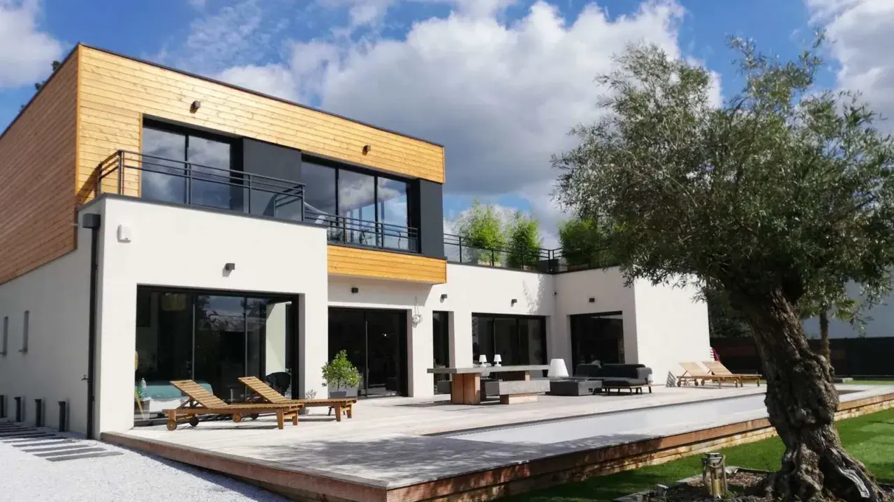 Maison moderne avec un style architectural audacieux, mêlant bois et blanc. Terrasse spacieuse avec mobilier extérieur et piscine.