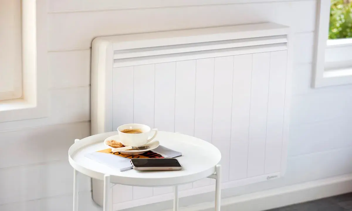 Un radiateur blanc moderne, idéal pour le chauffage maison neuve, avec une tasse de café et des magazines sur une table d'appoint.