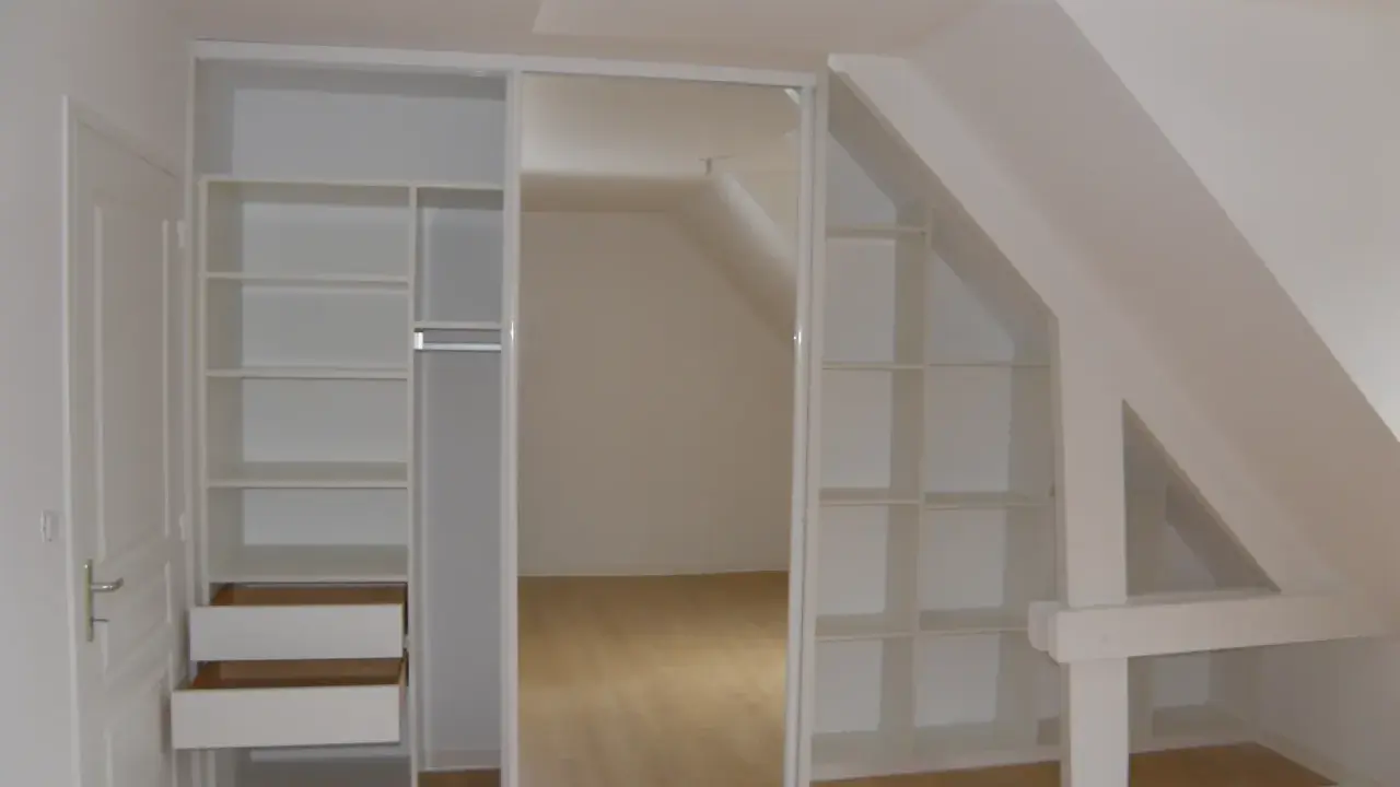 Aménagement astucieux pour faire un dressing sous pente. Étagères et tiroirs blancs s'intègrent parfaitement à l'espace mansardé.