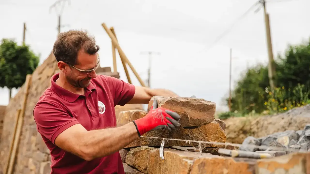 Un maçon, ganté de rouge, pose une pierre pour construire un mur en Corse.