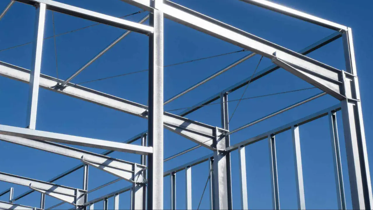 Structure métallique d'un bâtiment en construction, avec des poutres et des poteaux d'acier sous un ciel bleu clair.