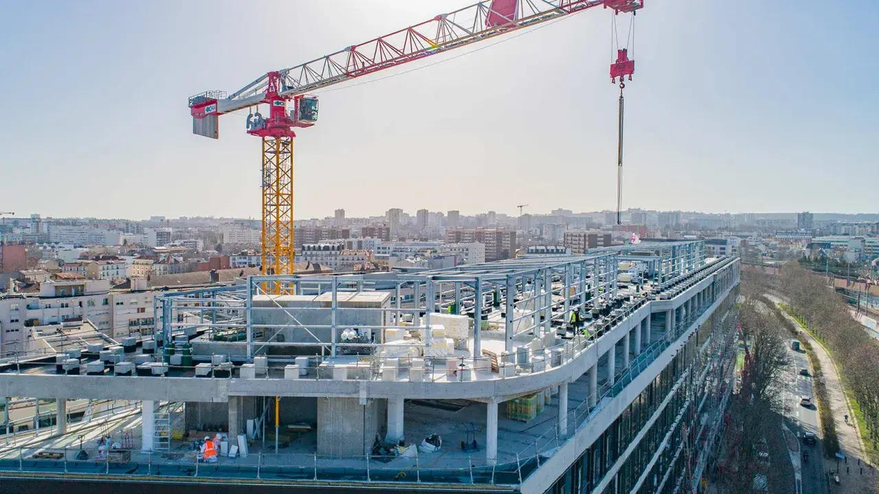 Grue de chantier sur un bâtiment en construction rapide, avec une ville en arrière-plan.