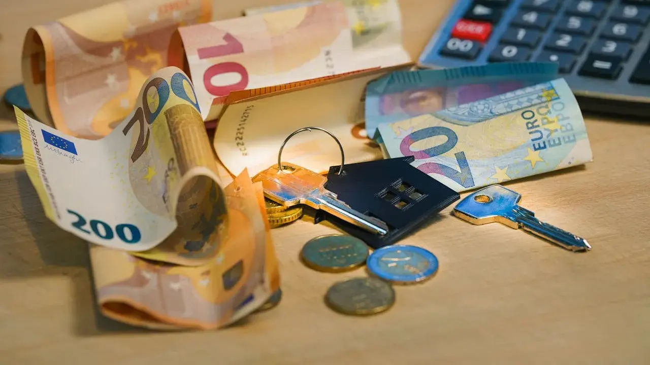 Clés, pièces et billets d'euros sur une table en bois. Calculatrice en arrière-plan. Le prix pose carrelage m2 est une préoccupation.