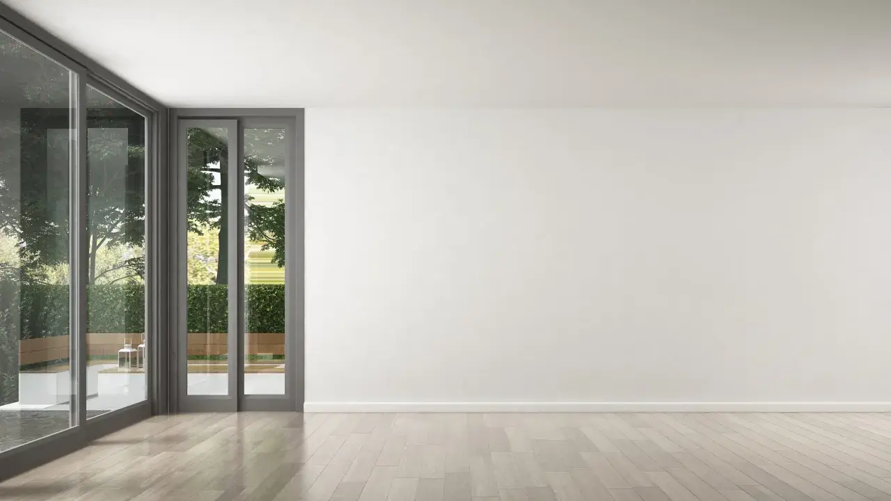 Un salon lumineux avec de grandes baies vitrées donnant sur un jardin verdoyant. Le parquet clair est parfait pour refaire le sol de la maison.