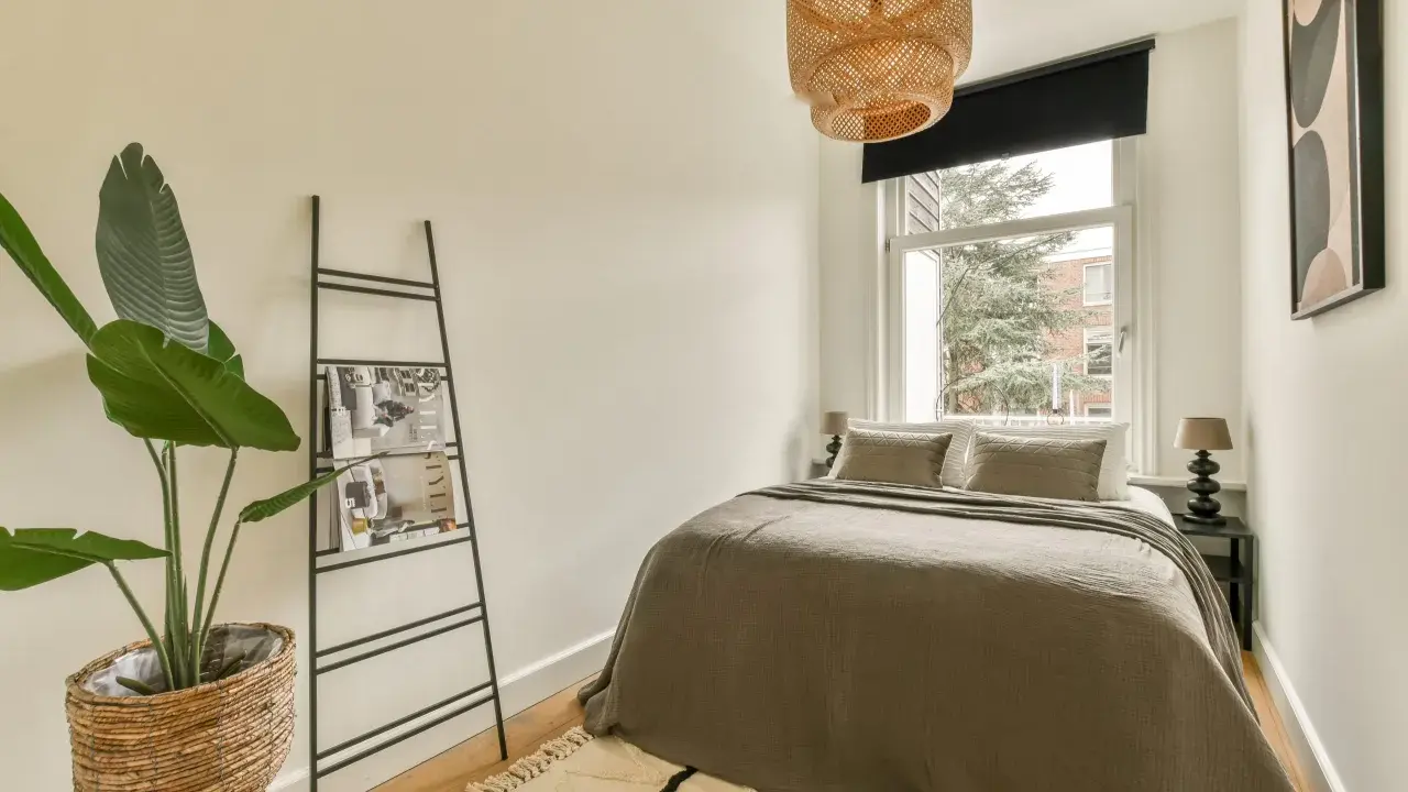 Chambre 9m2 avec salle de bain, lit douillet, plante verte et étagère murale. Luminaire en rotin au-dessus.