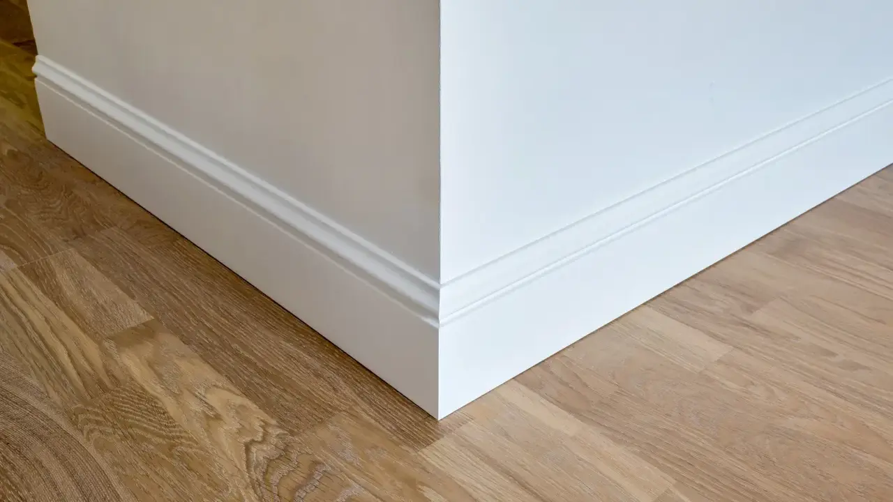 Un coin de mur blanc avec des plinthes moulurées et un parquet en bois clair. Ces plinthes servent à protéger les murs et à cacher les imperfections.