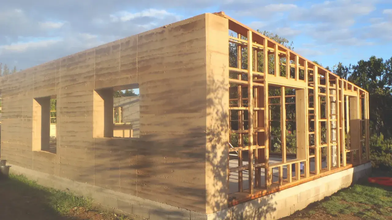 Construction d'une maison terre crue aux murs stratifiés, avec une ossature bois visible pour la suite.