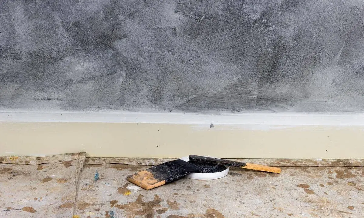 Outils pour enduire un mur abîmé : spatules et pot de mastic sur une bâche de protection au sol.