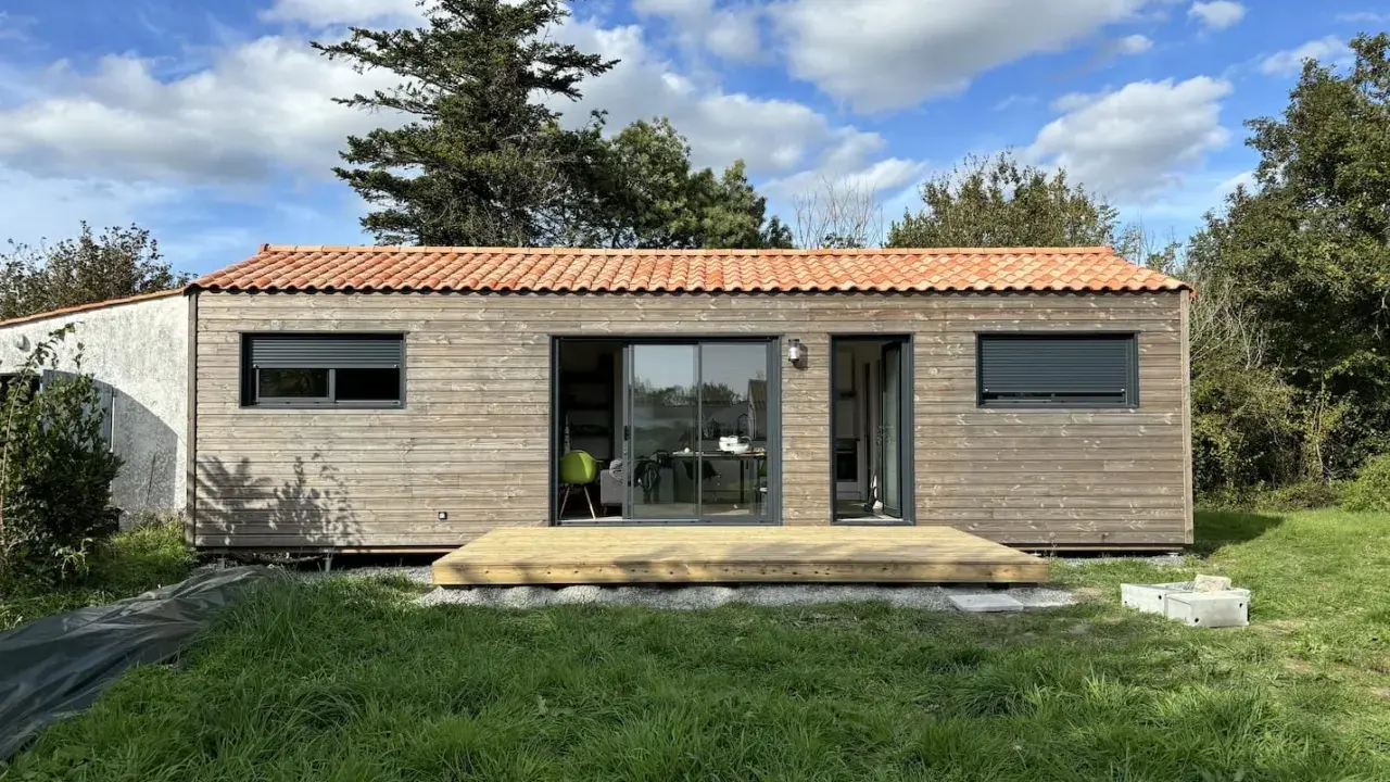 Une petite maison en bois avec une terrasse, idéale pour un plan maison 5m sur 10m. Le toit est couvert de tuiles rouges.