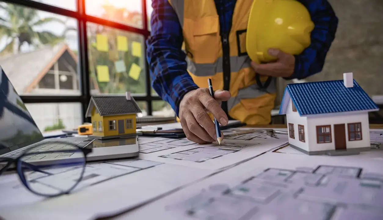 Un architecte examine des plans pour une maison ancienne, évaluant le DPE. Maquettes de maisons sur la table.