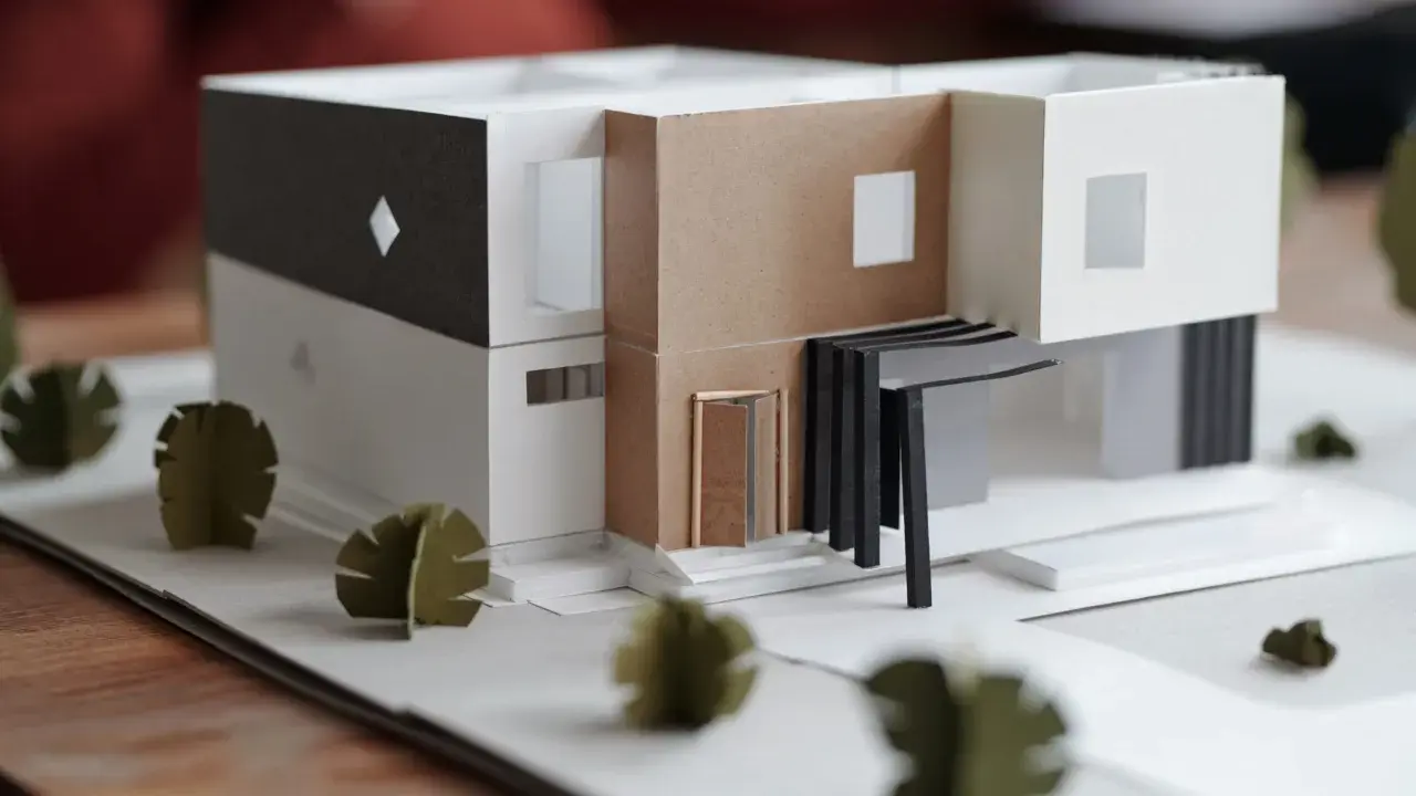 Maquette d'une maison individuelle moderne aux lignes épurées, avec des éléments en carton et des arbres stylisés.