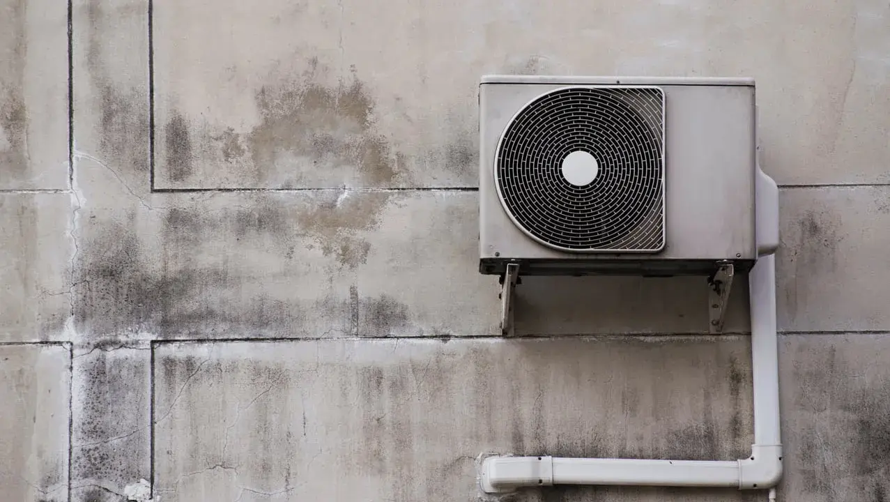 Unité extérieure d'une pompe à chaleur fixée sur un mur en béton. L'isolation est visible sur le tuyau blanc.