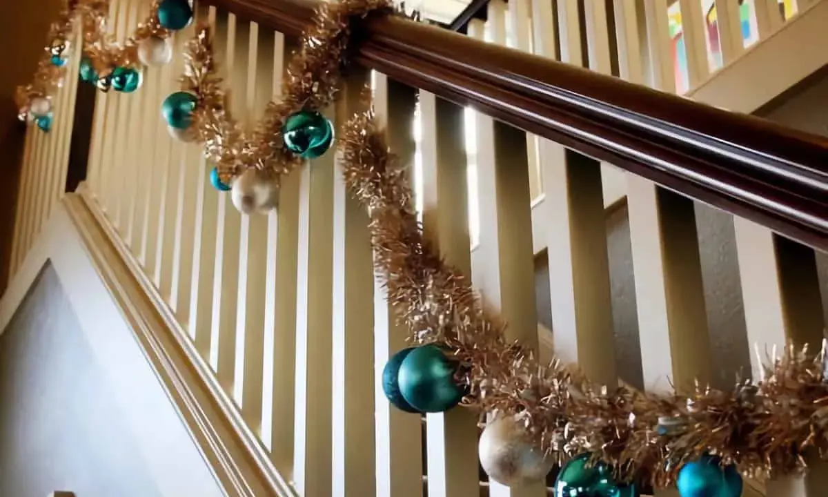 Guirlande dorée et boules de Noël bleues et blanches pour décorer une rampe d'escalier pour Noël.