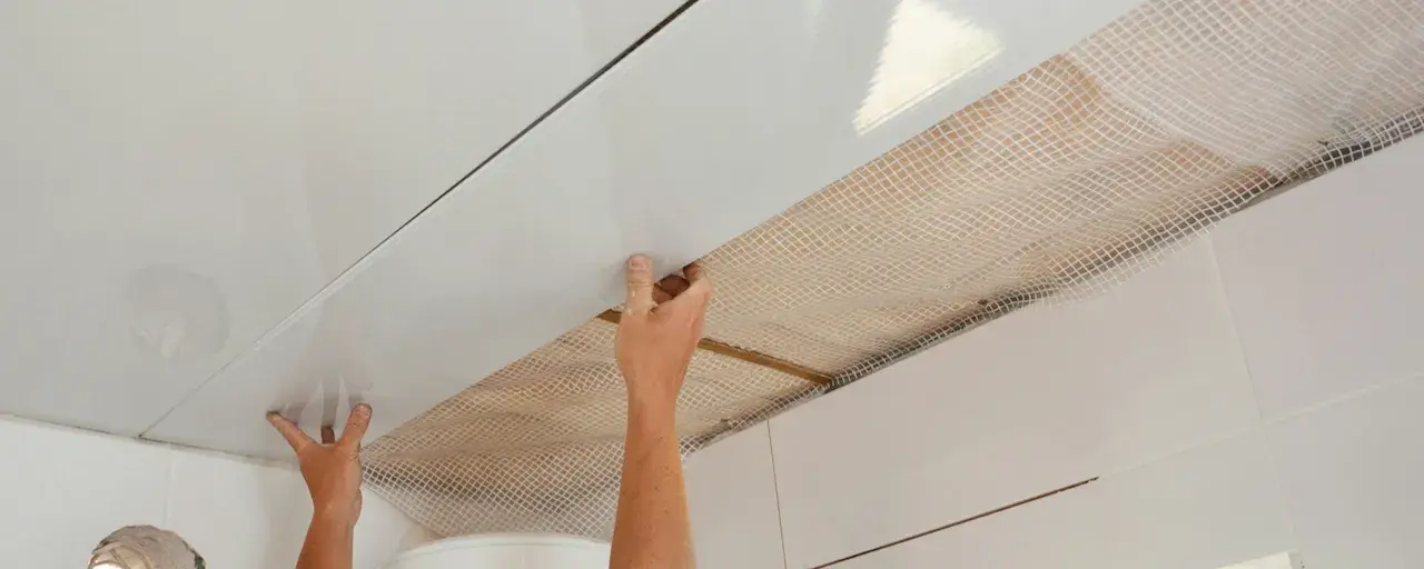 Mains installant des panneaux blancs pour refaire un plafond, avec un treillis visible en dessous.