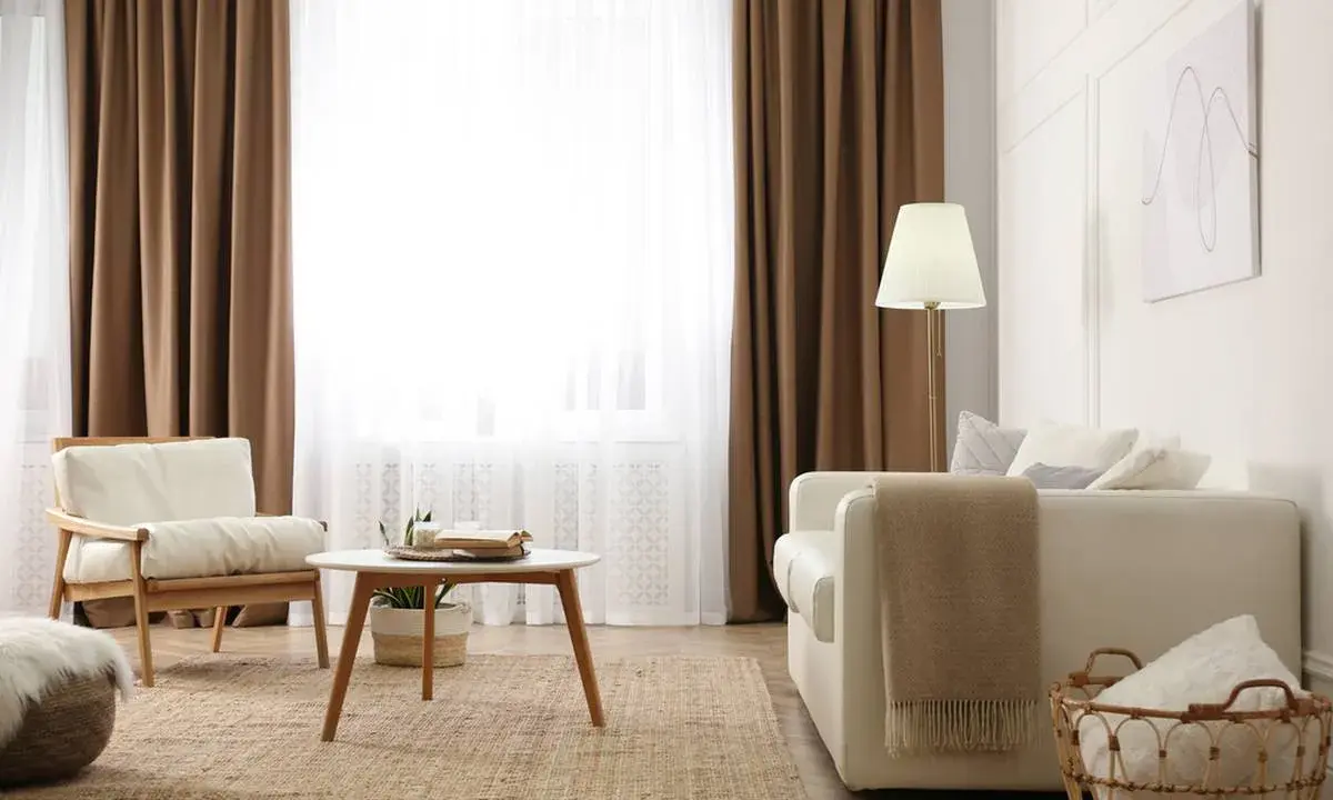 Salon cosy avec 1 ou 2 rideaux par fenêtre, fauteuil en bois, canapé blanc, table basse et tapis en jute.