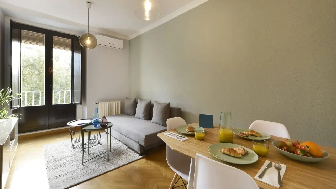 Un salon salle à manger de 20m2 prêt pour le petit-déjeuner, avec un canapé confortable, une table en bois garnie de croissants et de jus d'orange, et une grande fenêtre lumineuse.