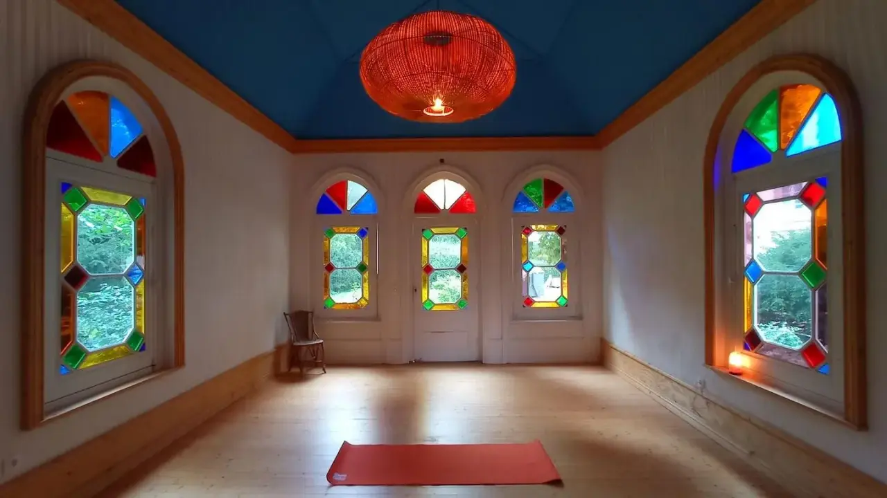 Un tapis de yoga orange attend dans une pièce lumineuse aux vitraux colorés, créant une atmosphère de maison bienveillante.