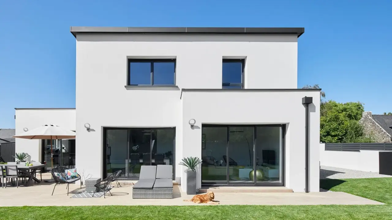 Maison moderne avec jardin, terrasse et chien. La ptz construction maison est visible sous un ciel bleu éclatant.