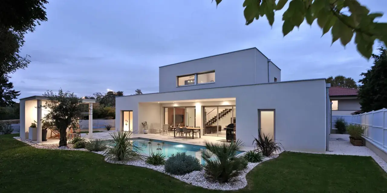 Vue arrière d'une maison moderne avec piscine illuminée, terrasse et jardin paysager. Un exemple de plan maison de luxe.