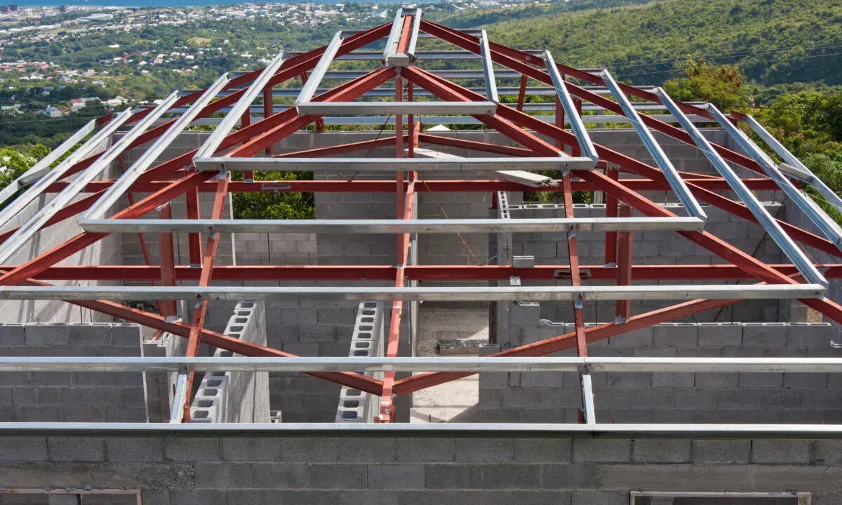 Structure métallique d'une maison en construction, avec des poutres rouges et grises. Un inconvénient potentiel de ce type de maison est la nécessité d'une isolation thermique soignée.