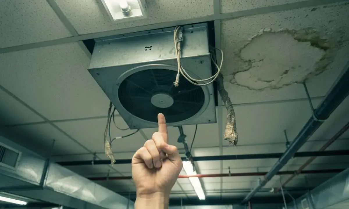 Une main pointe un VMC bruyant au plafond, à côté d'une tache d'humidité.