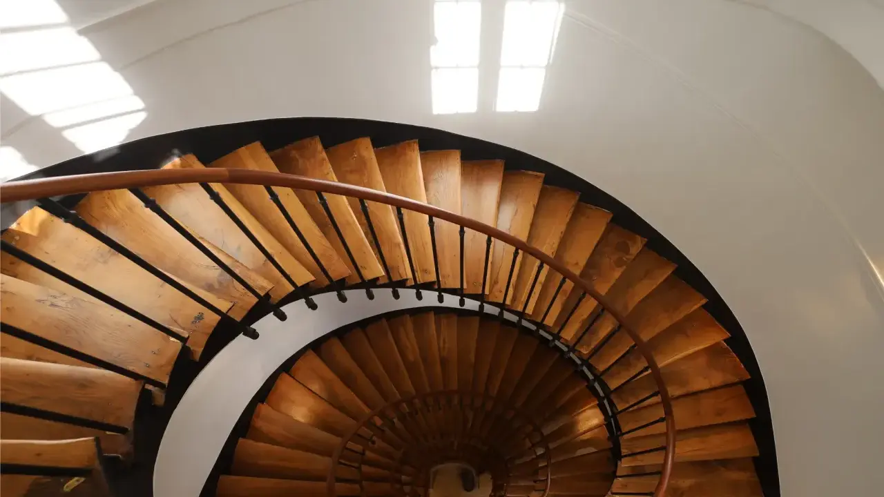 Vue plongeante d'un escalier en colimaçon en bois, parfait pour une rénovation cage escalier immeuble. La lumière naturelle illumine les marches.