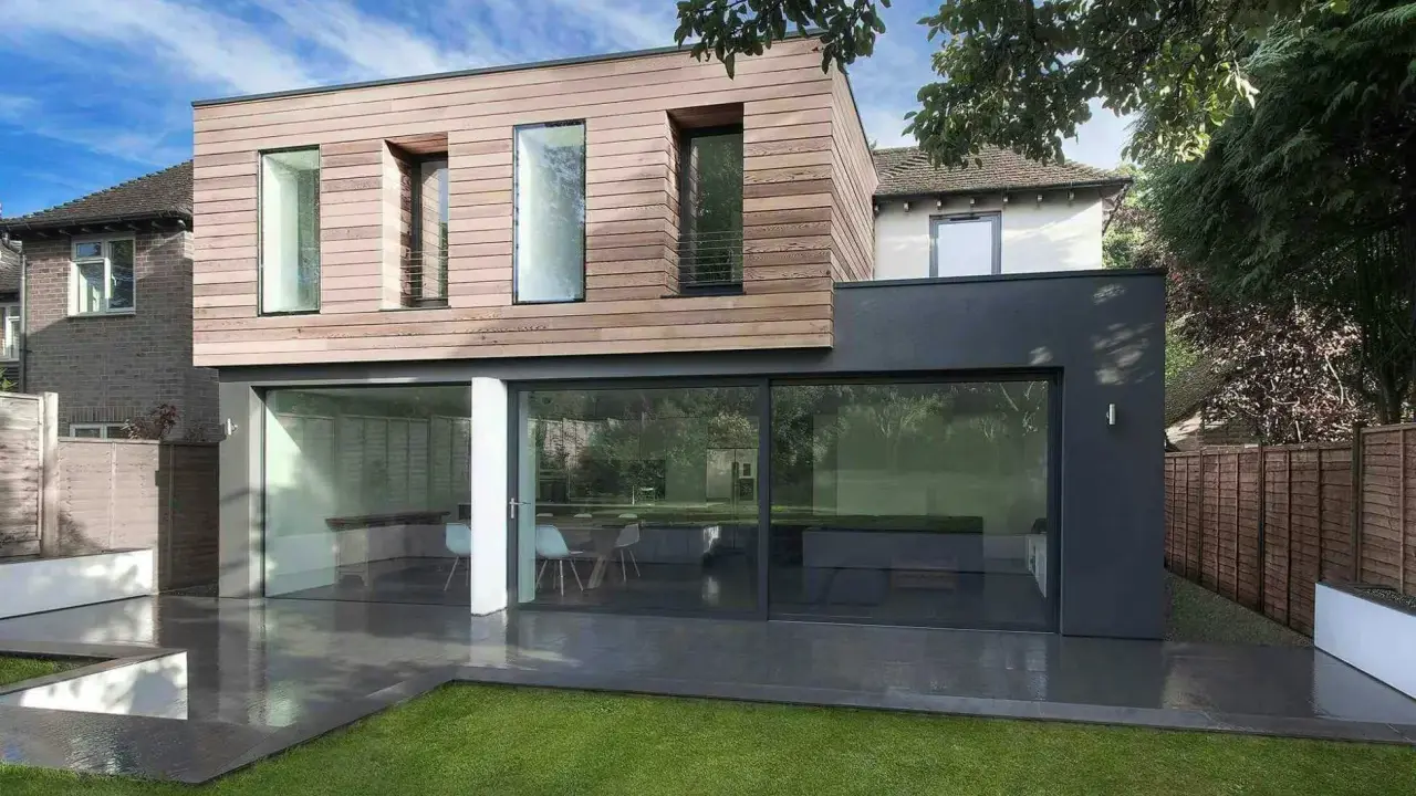 Une extension moderne en bois et anthracite pour agrandir une maison, avec de grandes baies vitrées donnant sur un jardin.