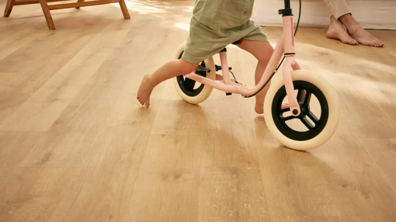 Un enfant apprend à faire du vélo d'équilibre sur un sol de salle de jeux en bois clair.
