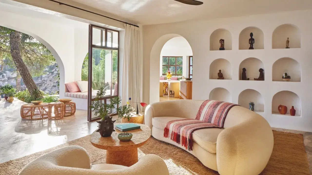 Comment habiller un mur blanc salon : des niches décorées d'objets ethniques et de poteries, un canapé incurvé, des fauteuils bouclette, et une vue sur un jardin luxuriant.