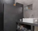 Salle de bain moderne avec murs en béton ciré. Une douche sans joint, un lavabo rectangulaire et des serviettes pliées créent une ambiance épurée.
