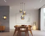 Quel luminaire pour salon salle à manger ? Suspensions modernes au-dessus d'une table en bois, lampe sur pied design et applique murale sphérique créent une ambiance chaleureuse.