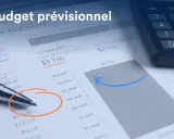 Un stylo sur un budget prévisionnel, avec une calculatrice. Le budget est en cours de construction, avec des chiffres et un graphique.