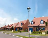 Vue d'une rue bordée de maisons de lotissement aux toits rouges et volets bleus, sous un ciel d'été.