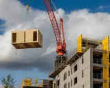 Une grue rouge soulève un module en bois pour la construction hors site d'un bâtiment en béton.