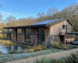 Une maison écologique moderne avec un toit végétalisé et des panneaux solaires, nichée près d'un étang gelé.