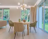 Éclairage salle à manger sans plafonnier : suspension moderne au-dessus d'une table ronde, entourée de chaises vertes. Lumière naturelle abondante des grandes fenêtres.