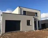 Maison moderne avec garage intégré. La couleur façade maison est un gris clair, contrastant avec des touches de blanc cassé et un bandeau de briques sombres.