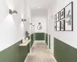 Un couloir moderne avec un soubassement vert, des appliques murales, une étagère en bois et des cadres photo.